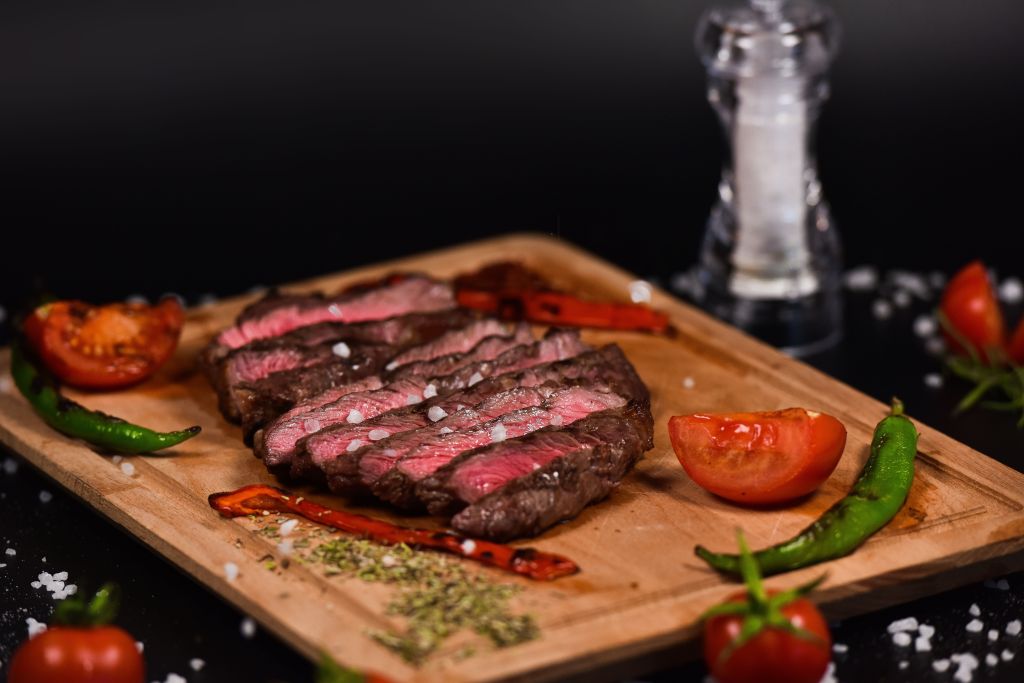 Carne a la parrilla cortada sobre una tabla de madera con tomates y pimientos